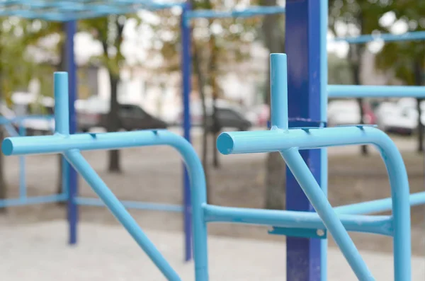 Sports bars in blue on the background of a street sports ground for training in athletics. Outdoor athletic gym equipment. Macro photo with selective focus and extremely blurred background