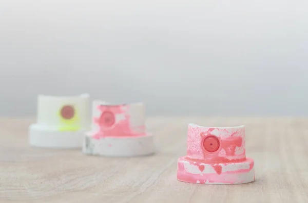 Several plastic nozzles from a paint sprayer that lie on a wooden surface against a gray wall background. The caps are smeared in fluorescent paint. The concept of street art and graffiti