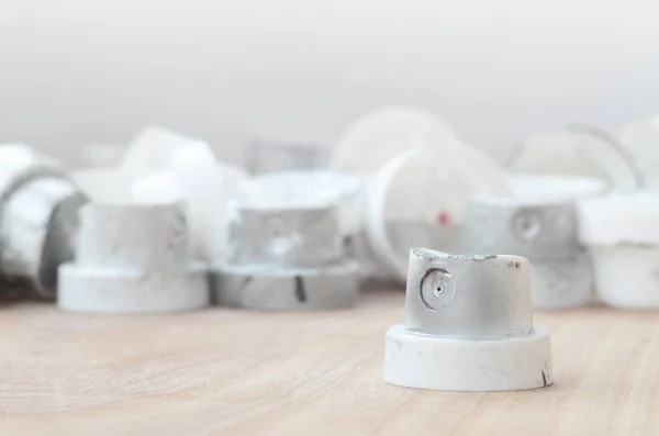 Several plastic nozzles from a paint sprayer that lie on a wooden surface against a gray wall background. The caps are smeared in chrome paint. The concept of street art and graffiti