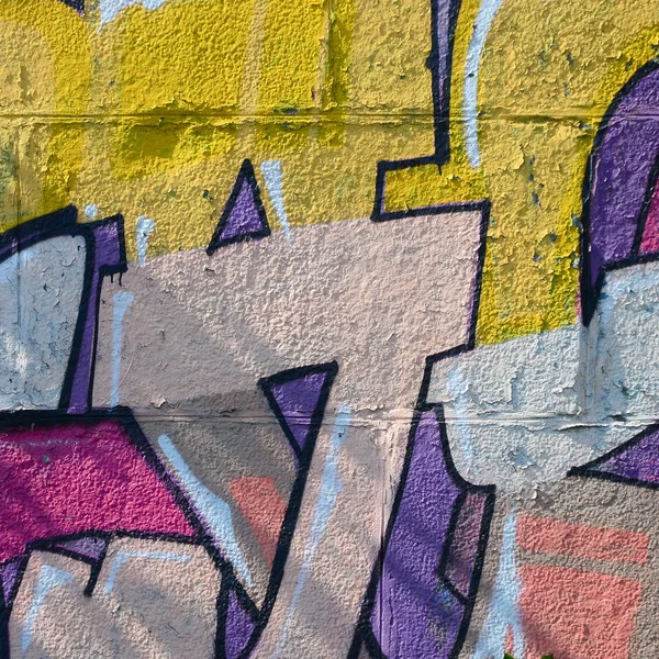 Fragment of graffiti drawings. The old wall decorated with paint stains in the style of street art culture. Colored background texture in warm tones.