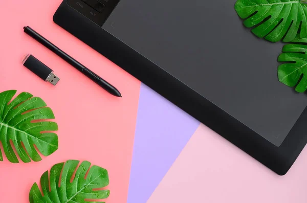 Graphic tablet and pen for illustrators and designers lies with USB memory card and monstera leafs on pastel background. Flat lay minimalism. Top view