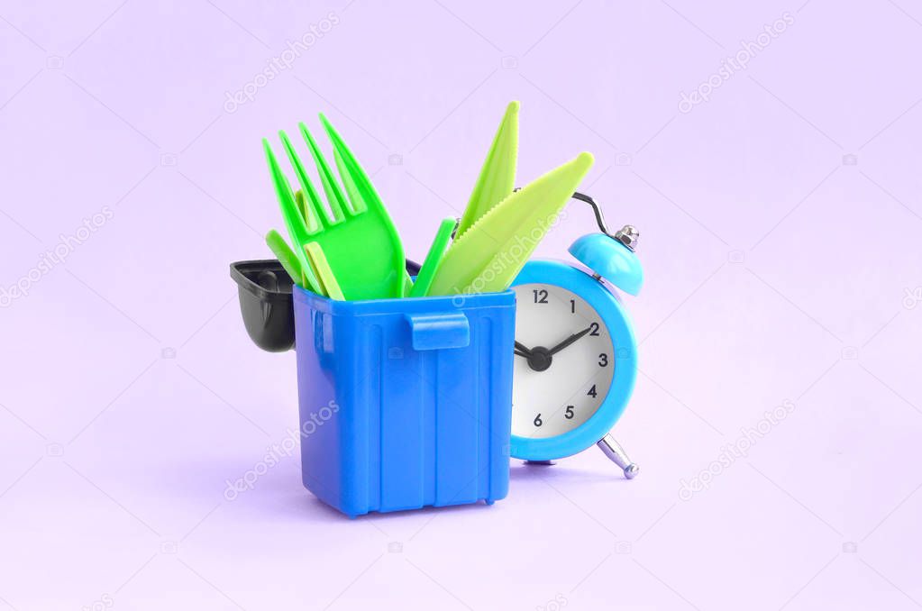 Alarm clock and plastic cutlery in trash bin on pink background. Time to say no to plastic cutlery. Plastic Pollution and Environmental Protection Concept. Eco Friendly