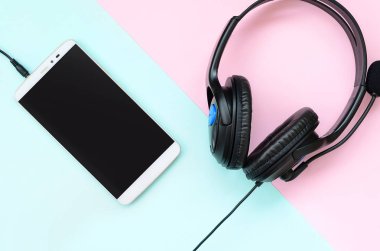Siyah kulaklık ve smartphone bir renkli pastel menekşe arka plan üzerinde yer almaktadır. Müzik dinleme konsepti. Taşınabilir teknoloji. Düz yatıyordu üstten görünüm