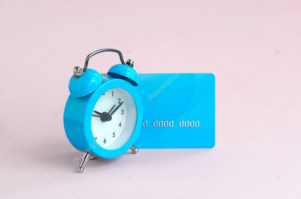 Small blue alarm clock is next to blue credit card. The concept of modern fast online banking and instant financial operations