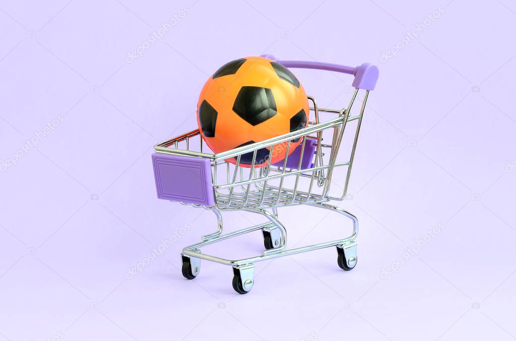 Orange soccer ball in shopping cart on violet. The concept of selling sports equipment, predictions for sports matches, sports betting