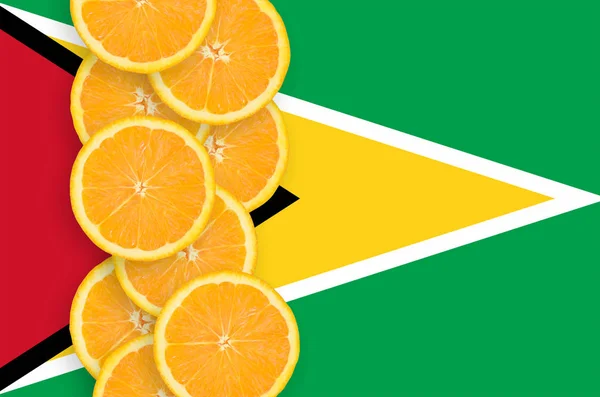 圭亚那国旗和垂直行的橙色柑橘水果片 柑橘类水果的种植及进出口概念 — 图库照片