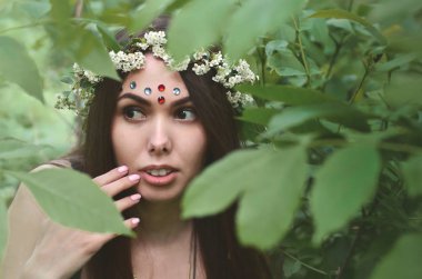 Güzel bir genç esmer koyu kahverengi gözleri ve büyük dudaklar ile Avrupa görünüm bir orman resim. Kızın üzerinde kafasını onun alnında parlak süslemeleri çiçek çelenk takarak
