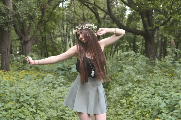 A forest picture of a beautiful young brunette of European appearance with dark brown eyes and large lips. On the girl's head is wearing a floral wreath, on her forehead shiny decorations