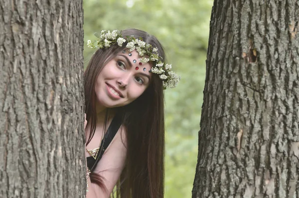 A forest picture of a beautiful young brunette of European appearance with dark brown eyes and large lips. On the girl\'s head is wearing a floral wreath, on her forehead shiny decorations