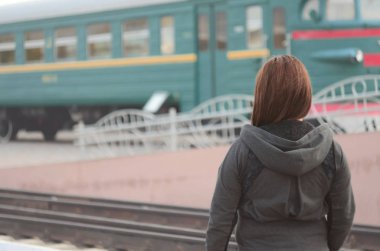 Kızıl saçlı bir kız demiryolu platformu üzerinde duran ve çıkış yapan tren izliyor. Treni için geç bir kadındı. Arkadan Görünüm