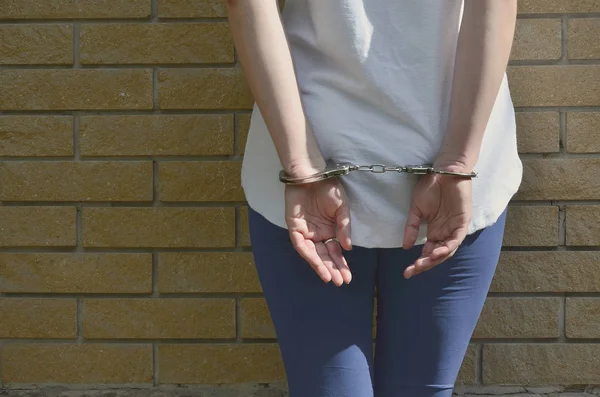 一个年轻的犯罪女孩的身体碎片与手在一个黄色的砖墙背景手铐 城市环境中女性犯罪嫌疑人的羁押理念 — 图库照片
