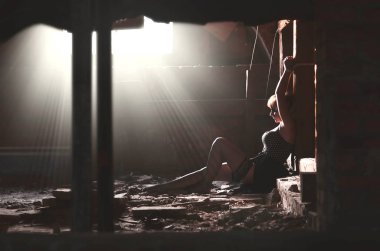 Terk edilmiş bir binada eski bir tavan arasında oturan bir ahşap direk kız bağlı. Güzel genç sarışın kız siyah elbise ve çorap elleri bağlı ile rehin