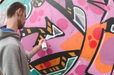 Gri kapüşonlu genç bir adam, yağmurlu havalarda grafiti bir duvar pembe ve yeşil renklerde boyar. Balıkgözü atış
