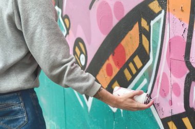 El gri kapüşonlu genç bir adamın grafiti bir duvar pembe ve yeşil renklerde yağmurlu havalarda boyar.
