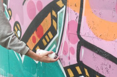 El gri kapüşonlu genç bir adamın grafiti bir duvar pembe ve yeşil renklerde yağmurlu havalarda boyar.
