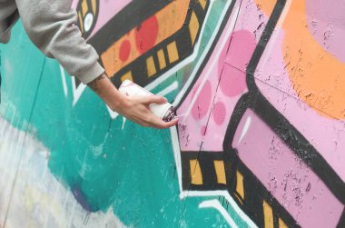 El gri kapüşonlu genç bir adamın grafiti bir duvar pembe ve yeşil renklerde yağmurlu havalarda boyar.