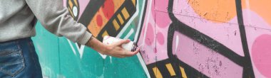 El gri kapüşonlu genç bir adamın grafiti bir duvar pembe ve yeşil renklerde yağmurlu havalarda boyar.