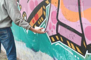 El gri kapüşonlu genç bir adamın grafiti bir duvar pembe ve yeşil renklerde yağmurlu havalarda boyar.