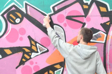 Gri kapüşonlu genç bir adam grafiti bir duvar pembe ve yeşil renklerde yağmurlu havalarda boyar.
