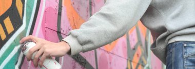 Gri kapüşonlu genç bir adam grafiti bir duvar pembe ve yeşil renklerde yağmurlu havalarda boyar.