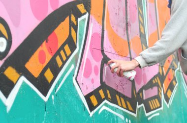 El gri kapüşonlu genç bir adamın grafiti bir duvar pembe ve yeşil renklerde yağmurlu havalarda boyar.