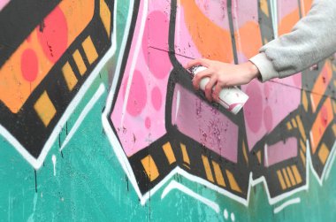 El gri kapüşonlu genç bir adamın grafiti bir duvar pembe ve yeşil renklerde yağmurlu havalarda boyar.