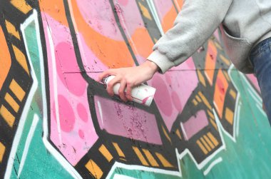 El gri kapüşonlu genç bir adamın grafiti bir duvar pembe ve yeşil renklerde yağmurlu havalarda boyar.