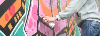 El gri kapüşonlu genç bir adamın grafiti bir duvar pembe ve yeşil renklerde yağmurlu havalarda boyar.