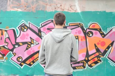 Gri kapüşonlu bir genç grafiti sanatçısı bir duvara yağmurlu havalarda pembe ve yeşil renklerde onun graffiti ile duvara görünüyor. Sokak sanatı kavramı