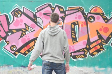 Gri kapüşonlu bir genç grafiti sanatçısı bir duvara yağmurlu havalarda pembe ve yeşil renklerde onun graffiti ile duvara görünüyor. Sokak sanatı kavramı