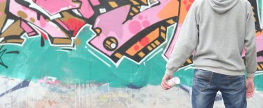 Gri kapüşonlu bir genç grafiti sanatçısı bir duvara yağmurlu havalarda pembe ve yeşil renklerde onun graffiti ile duvara görünüyor. Sokak sanatı kavramı