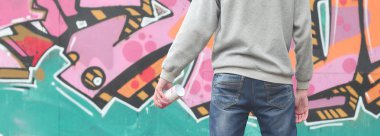 Gri kapüşonlu bir genç grafiti sanatçısı bir duvara yağmurlu havalarda pembe ve yeşil renklerde onun graffiti ile duvara görünüyor. Sokak sanatı kavramı
