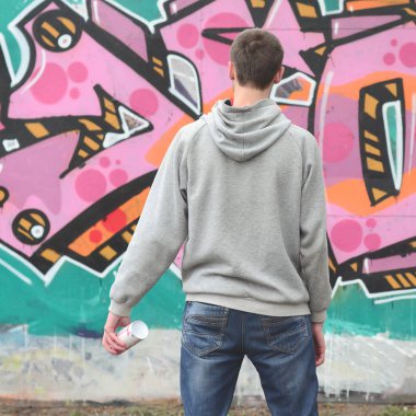 Gri kapüşonlu bir genç grafiti sanatçısı bir duvara yağmurlu havalarda pembe ve yeşil renklerde onun graffiti ile duvara görünüyor. Sokak sanatı kavramı