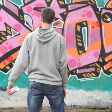 Gri kapüşonlu bir genç grafiti sanatçısı bir duvara yağmurlu havalarda pembe ve yeşil renklerde onun graffiti ile duvara görünüyor. Sokak sanatı kavramı