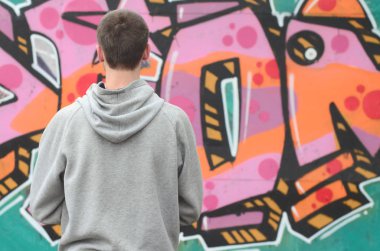 Gri kapüşonlu bir genç grafiti sanatçısı bir duvara yağmurlu havalarda pembe ve yeşil renklerde onun graffiti ile duvara görünüyor. Sokak sanatı kavramı