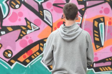 Gri kapüşonlu bir genç grafiti sanatçısı bir duvara yağmurlu havalarda pembe ve yeşil renklerde onun graffiti ile duvara görünüyor. Sokak sanatı kavramı