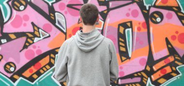 Gri kapüşonlu bir genç grafiti sanatçısı bir duvara yağmurlu havalarda pembe ve yeşil renklerde onun graffiti ile duvara görünüyor. Sokak sanatı kavramı