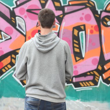 Gri kapüşonlu bir genç grafiti sanatçısı bir duvara yağmurlu havalarda pembe ve yeşil renklerde onun graffiti ile duvara görünüyor. Sokak sanatı kavramı