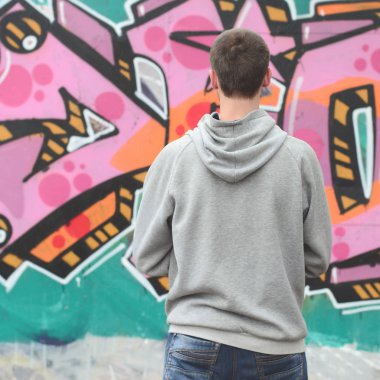 Gri kapüşonlu bir genç grafiti sanatçısı bir duvara yağmurlu havalarda pembe ve yeşil renklerde onun graffiti ile duvara görünüyor. Sokak sanatı kavramı
