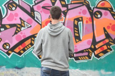 Gri kapüşonlu bir genç grafiti sanatçısı bir duvara yağmurlu havalarda pembe ve yeşil renklerde onun graffiti ile duvara görünüyor. Sokak sanatı kavramı