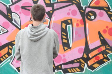 Gri kapüşonlu bir genç grafiti sanatçısı bir duvara yağmurlu havalarda pembe ve yeşil renklerde onun graffiti ile duvara görünüyor. Sokak sanatı kavramı