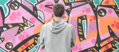 Gri kapüşonlu bir genç grafiti sanatçısı bir duvara yağmurlu havalarda pembe ve yeşil renklerde onun graffiti ile duvara görünüyor. Sokak sanatı kavramı