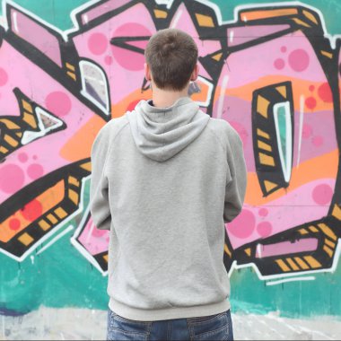 Gri kapüşonlu bir genç grafiti sanatçısı bir duvara yağmurlu havalarda pembe ve yeşil renklerde onun graffiti ile duvara görünüyor. Sokak sanatı kavramı