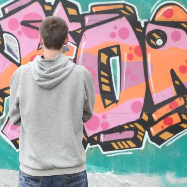Gri kapüşonlu bir genç grafiti sanatçısı bir duvara yağmurlu havalarda pembe ve yeşil renklerde onun graffiti ile duvara görünüyor. Sokak sanatı kavramı