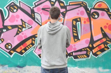 Gri kapüşonlu bir genç grafiti sanatçısı bir duvara yağmurlu havalarda pembe ve yeşil renklerde onun graffiti ile duvara görünüyor. Sokak sanatı kavramı