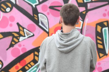 Gri kapüşonlu bir genç grafiti sanatçısı bir duvara yağmurlu havalarda pembe ve yeşil renklerde onun graffiti ile duvara görünüyor. Sokak sanatı kavramı