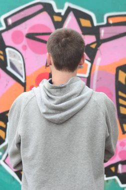 Gri kapüşonlu bir genç grafiti sanatçısı bir duvara yağmurlu havalarda pembe ve yeşil renklerde onun graffiti ile duvara görünüyor. Sokak sanatı kavramı