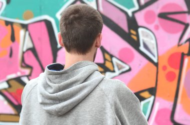 Gri kapüşonlu bir genç grafiti sanatçısı bir duvara yağmurlu havalarda pembe ve yeşil renklerde onun graffiti ile duvara görünüyor. Sokak sanatı kavramı