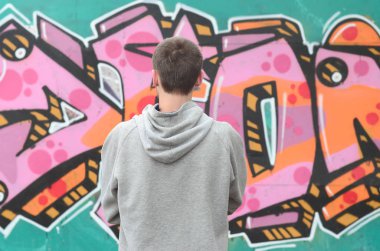 Gri kapüşonlu bir genç grafiti sanatçısı bir duvara yağmurlu havalarda pembe ve yeşil renklerde onun graffiti ile duvara görünüyor. Sokak sanatı kavramı