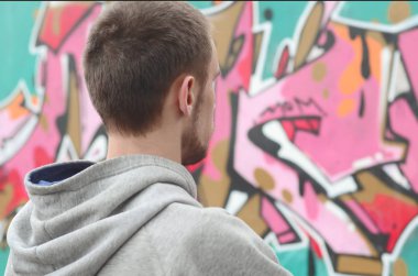 Gri kapüşonlu bir genç grafiti sanatçısı bir duvara yağmurlu havalarda pembe ve yeşil renklerde onun graffiti ile duvara görünüyor. Sokak sanatı kavramı